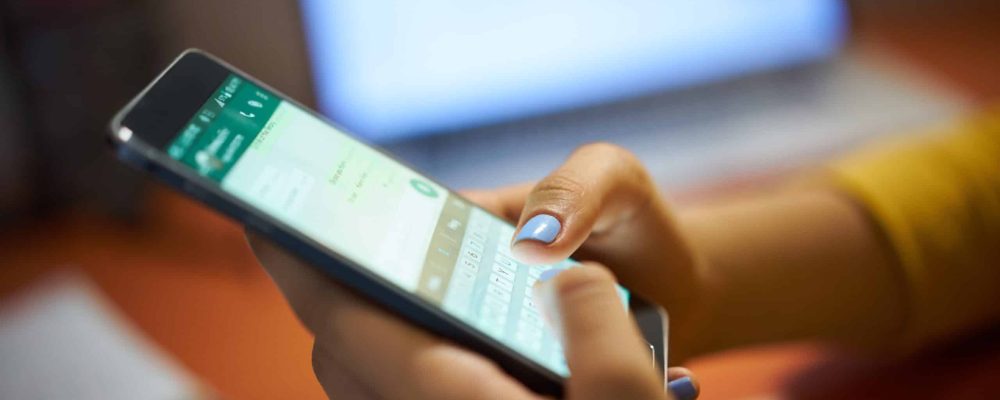 Girl Typing Phone Message On Social Network At Night Young woman using cell phone to send text message on social network at night. Closeup of hands with computer laptop in background